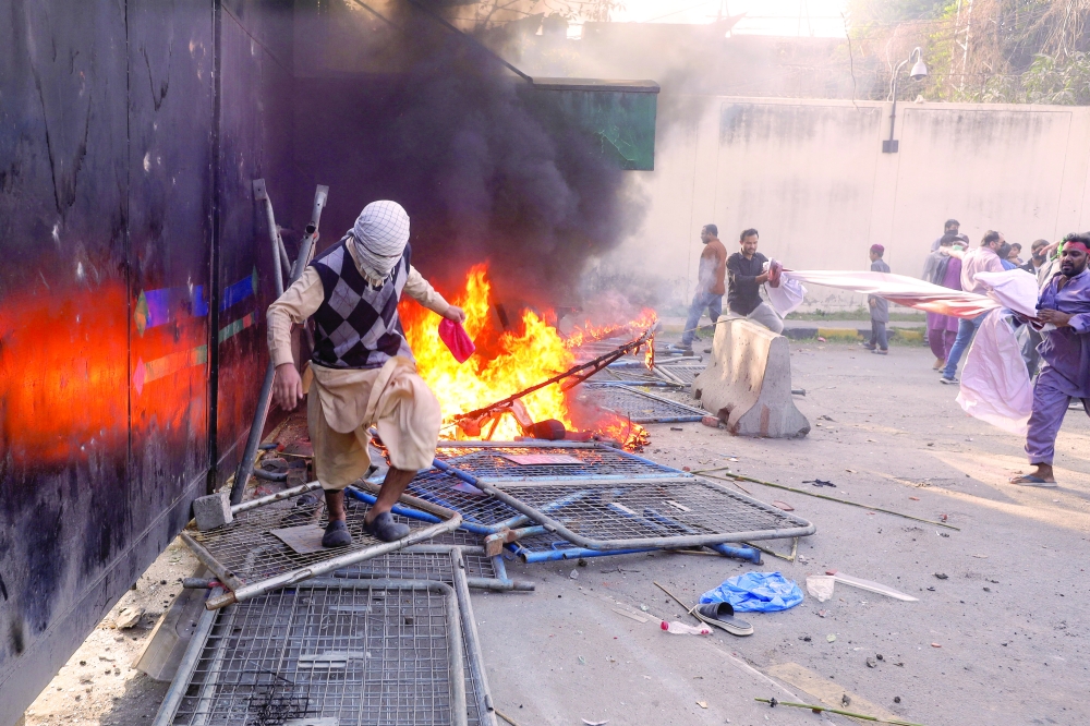 A protester sets fire near a gate leading to the US Consulate during a violent protest in Lahore, Pakistan. — Reuters