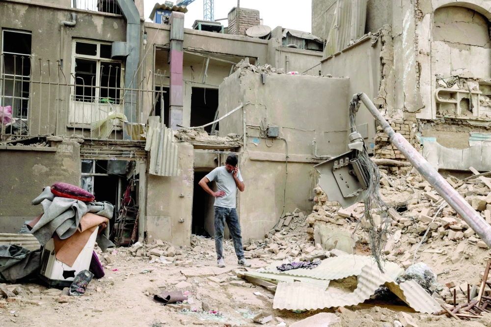 A man speaks on a mobile phone as he stands outside damaged homes, in Tehran. — AFP