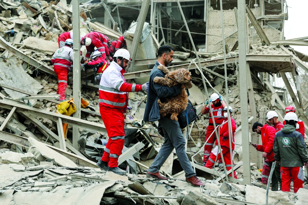A man carries a dog as emergency personnel work at the site of a strike on a residential building, in Tehran. — Reuters